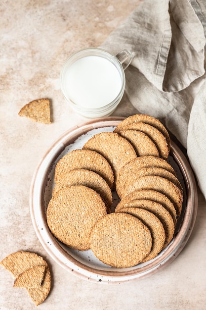 Tasty crackers with seeds on a plate and a cup of milk brown background Snack or breakfast