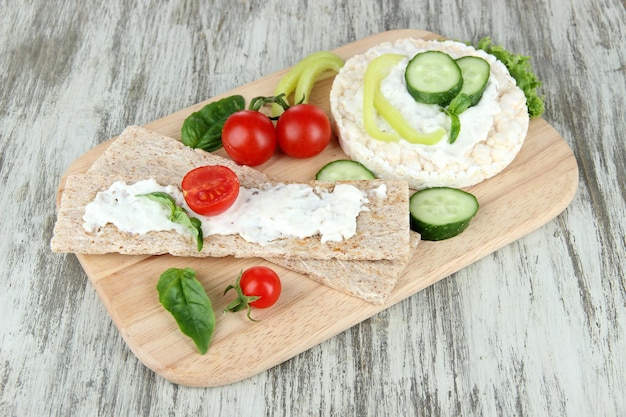 Tasty crispbreads with vegetables on wooden background