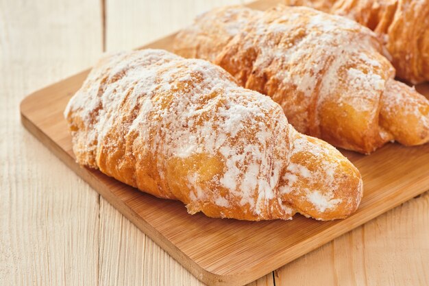 Tasty croissants with powdered sugar on wooden board. Traditional french pastry on the breakfast. Close up view