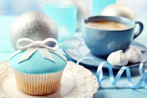 Tasty cupcake with bow, coffee cup and Christmas toys on color wooden background