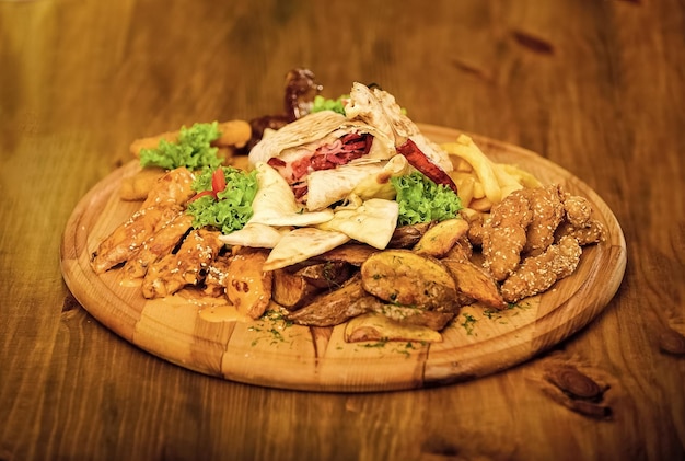 Tasty delicious snacks Restaurant food Snack for beer Wooden board with lot french fries fish sticks burrito and meat steak served with salad Pub menu snack High calorie snack for group friends