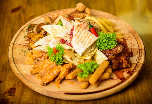 Tasty delicious snacks Snack for beer Restaurant food Wooden board with lot french fries fish sticks burrito and meat steak served with salad High calorie snack for group friends Pub menu snack