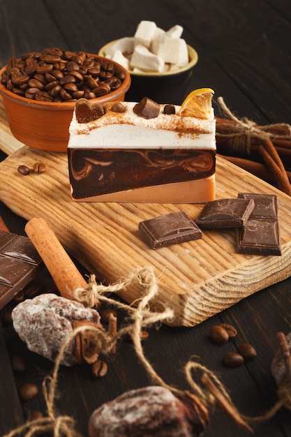 Tasty dessert background. Cake piece, chocolate bars, refined sugar, coffee beans, cinnamon and dry persimmon on rustic wooden table, side view. Advertizing design