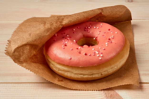 Tasty donut with pink icing, colored sugar sprinkles on wooden background