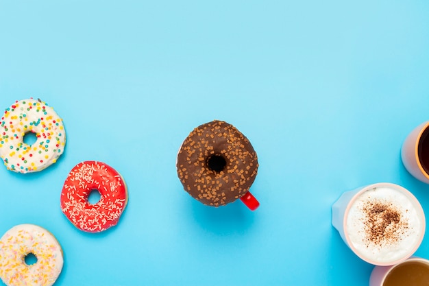 Tasty donuts and cups with hot drinks on a blue surface. Concept of sweets, bakery, pastries, coffee shop. Square. Flat lay, top view