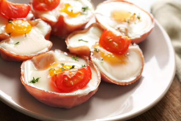 Tasty eggs with tomatoes in ham on plate closeup