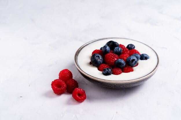 Tasty fresh blueberry raspberries yoghurt shake dessert in ceramic bowl standing on white table