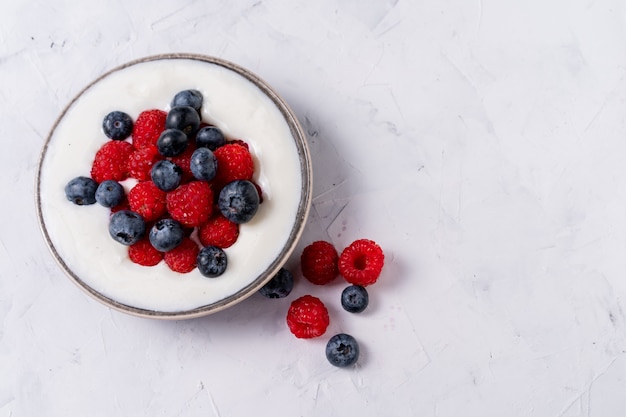 Tasty fresh blueberry raspberries yoghurt shake dessert in ceramic bowl standing on white table