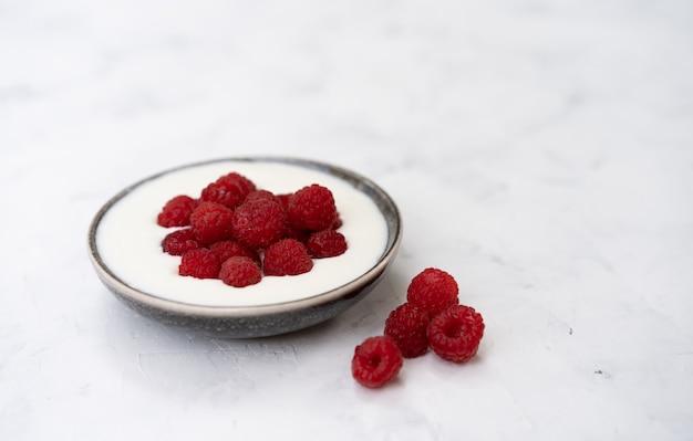 Tasty fresh raspberries yoghurt shake dessert in ceramic bowl standing on white table . Homemade berry smoothie. Healthy eating. Diet food.