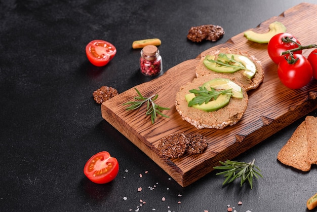 Tasty fresh sandwich with liver paste, avocado pieces and a arugula on a dark concrete table