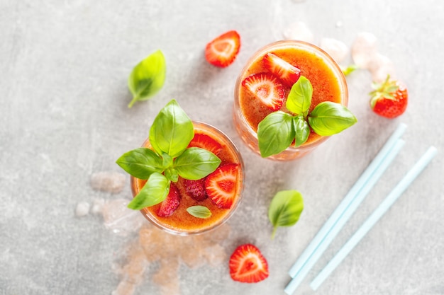 Tasty freshmade drink with stawberry and basil served in glasses on concrete table.