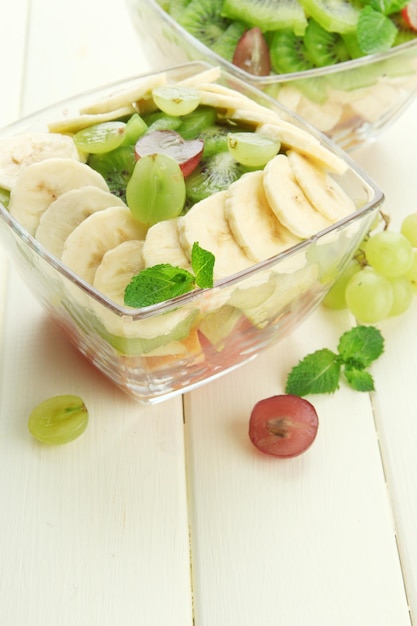 Tasty fruit salad in glass bowls on white wooden table