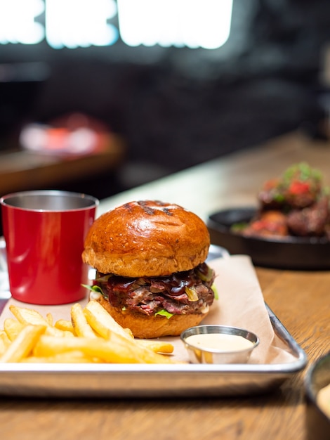 Tasty grilled burger and sauce on wooden table with french fries