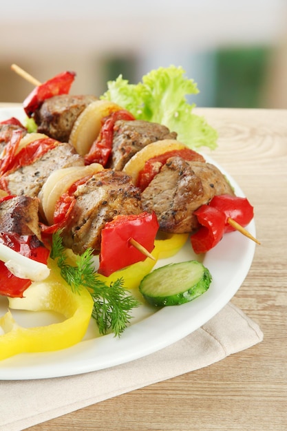 Tasty grilled meat and vegetables on skewer on plate on wooden table