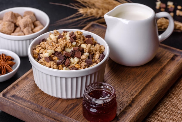 Tasty healthy breakfast with cereals granola chocolate milk and jam on a dark concrete background