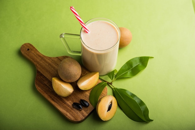 Tasty and healthy Chickoo, Chikoo OR Sapota Milkshake. It's a healthy fruit mixed with Milk and ice served in a glass over colourful or wooden background. Selective focus