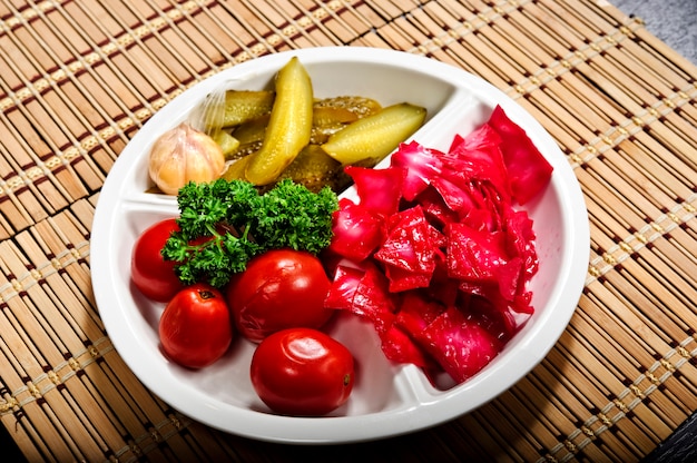 Tasty homemade pickled products on a plate sauerkraut, pickled tomatoes, pickle, swooden background. Ukrainian traditional meal.