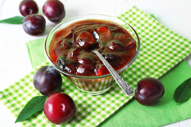 Tasty homemade plum jam in glass saucer on checkered napkin closeup