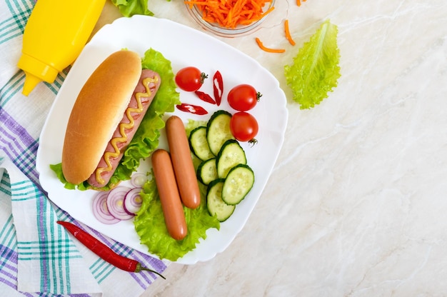 Tasty hot dogs with sausage grill, ketchup, mustard, lettuce, tomatoes on a white plate. The top view. Flat lay