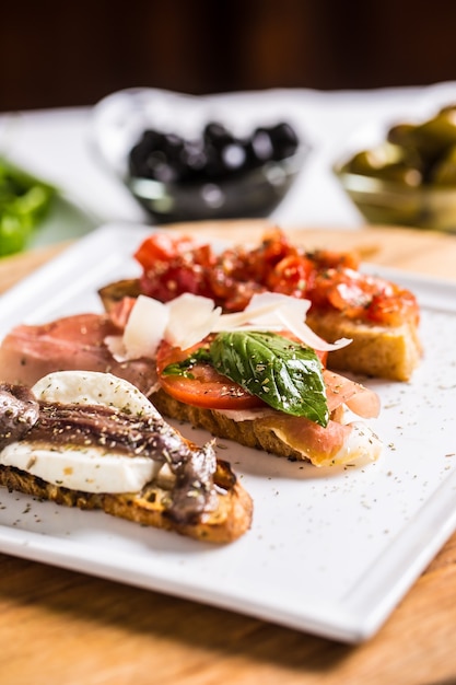 Tasty italian appetizer bruschettes with tomatoes anchovies prosciutto and mozarella.