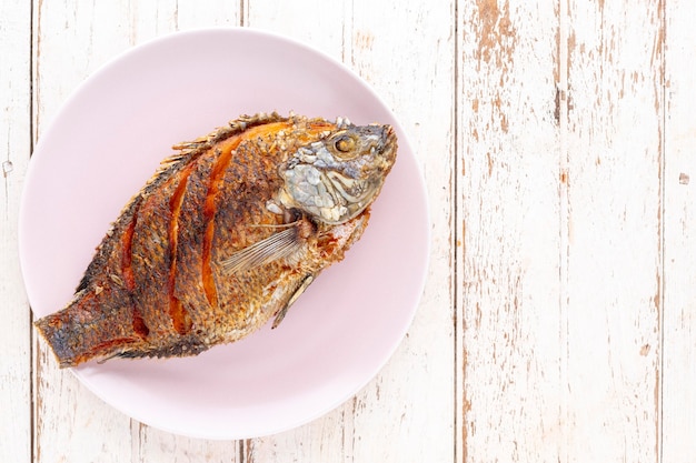 Tasty large fried nile tilapia fish in ceramic plate on white wooden texture background with copy space for text, top view, flat lay, light and airy food photography