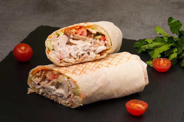 Tasty large Shawarma with vegetables and chicken on a dark background