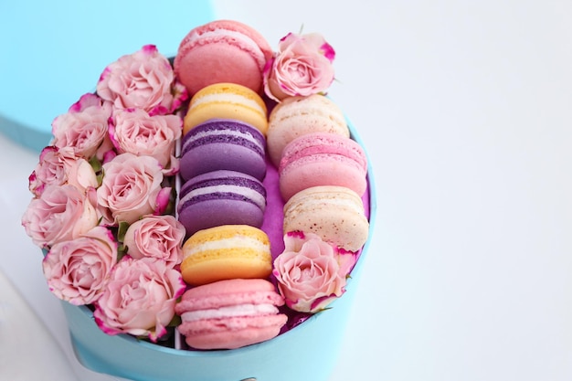 Tasty macaroons and roses in box on light background