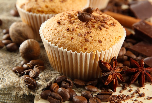 Tasty muffin cakes with chocolate, spices and coffee seeds, on beige background