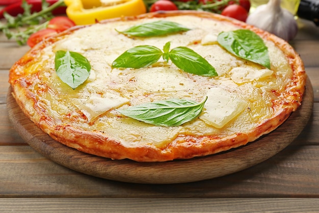 Tasty pizza decorated with basil and vegetables on wooden background close up