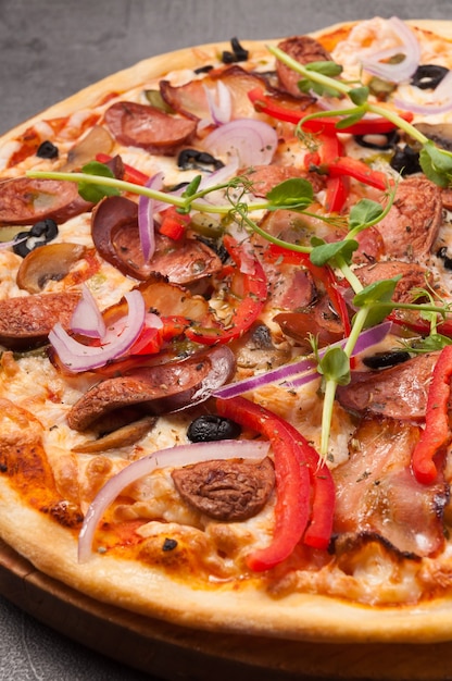 Tasty pizza with bacon and hunting sausages on a gray background close up