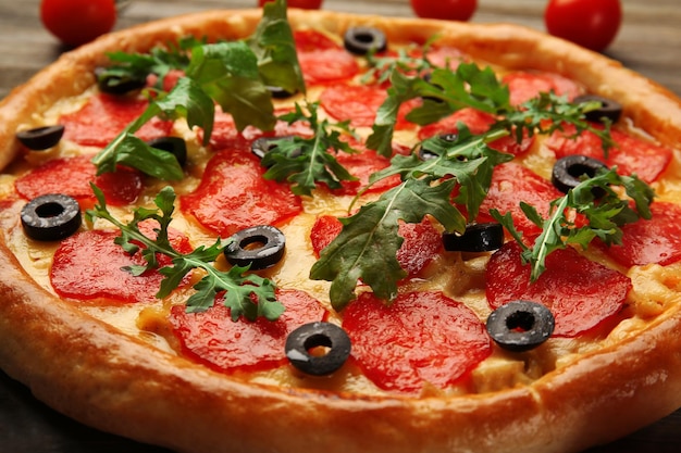 Tasty pizza with salami decorated with tomatoes on wooden background close up