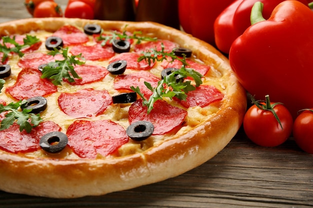 Tasty pizza with salami and red vegetables on wooden background close up