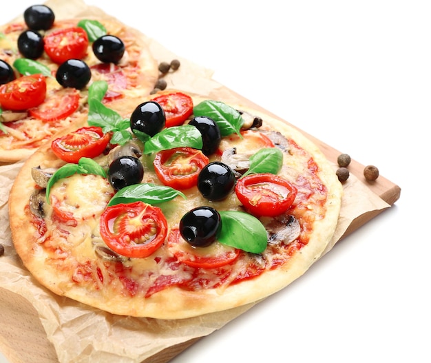 Tasty pizza with vegetables and basil on cutting board isolated on white