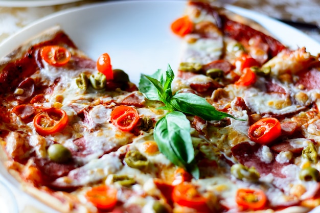 A tasty pizza with vegetables, meat, and sauces on a cafe on a white plate. Close up.