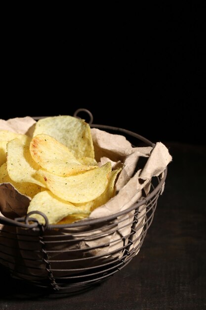 Tasty potato chips in metal basket on wooden table with dark light