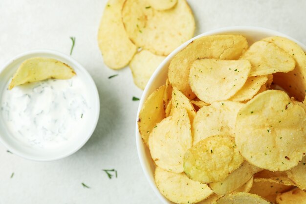 Tasty potato chips and sauce on white textured surface