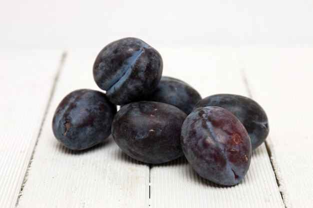 Tasty purple plums isolated on a white wooden background.