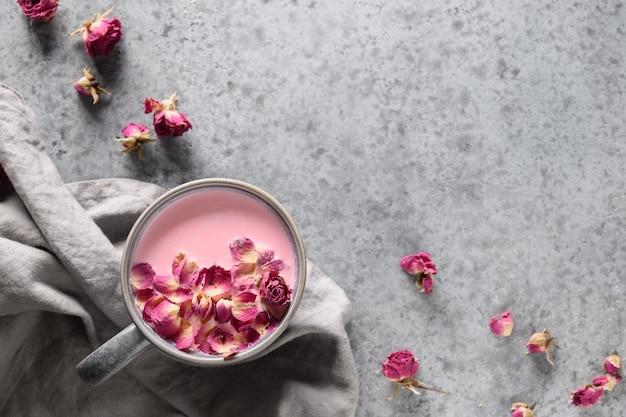 Tasty rose moon milk in grey cup and rose petals on grey background. View from above. Space for text.