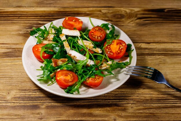 Tasty salad of fried chicken breast fresh arugula and cherry tomatoes on wooden table