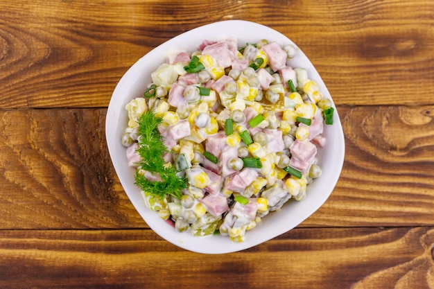 Tasty salad with sausage, green pea, canned corn, bell pepper, cucumber and mayonnaise on wooden table. Top view