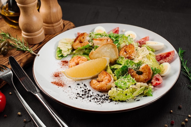 Tasty salad with shrimps herbs and vegetables on black background