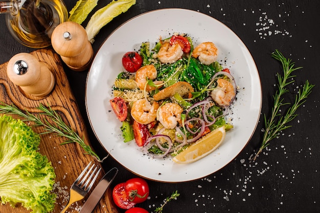 Tasty salad with shrimps herbs and vegetables on black background