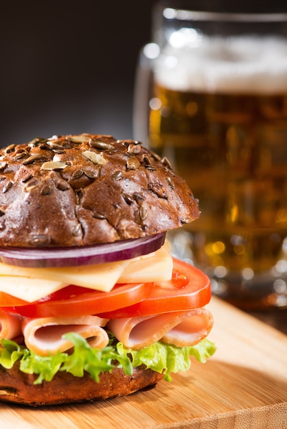 Tasty sandwich with green salad, meat, cheese and tomato with a beer mug