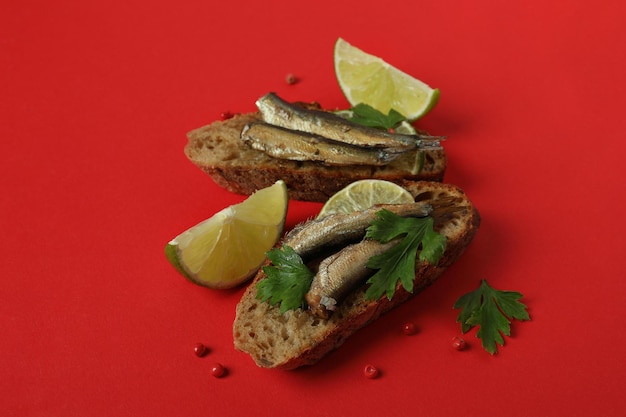 Tasty sandwiches with sprats on red background