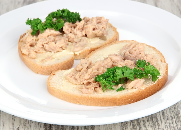 Tasty sandwiches with tuna and cod liver sardines on white plate on wooden background