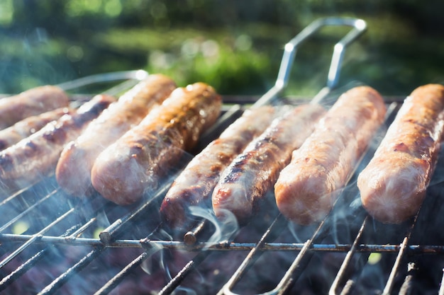 Tasty sausages grilling on portable barbecue on summer picnic Outdoors Smoke and fire Close up