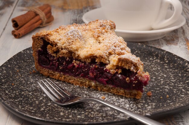 Tasty shortbread cherry pie on a dark plate with a Cup of tea