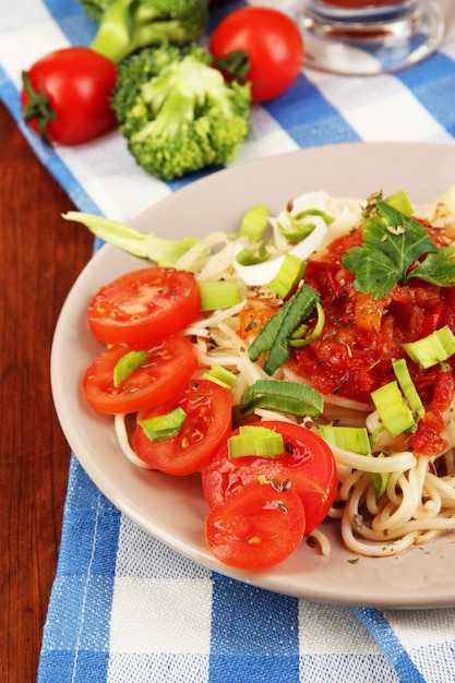 Tasty spaghetti with sauce and vegetables on plate on wooden table closeup