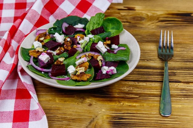 Tasty spinach salad with boiled beetroot feta cheese walnut and red onion on wooden table Healthy vegetarian food