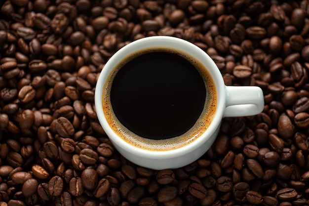 Tasty steaming espresso in cup with coffee beans. Closeup